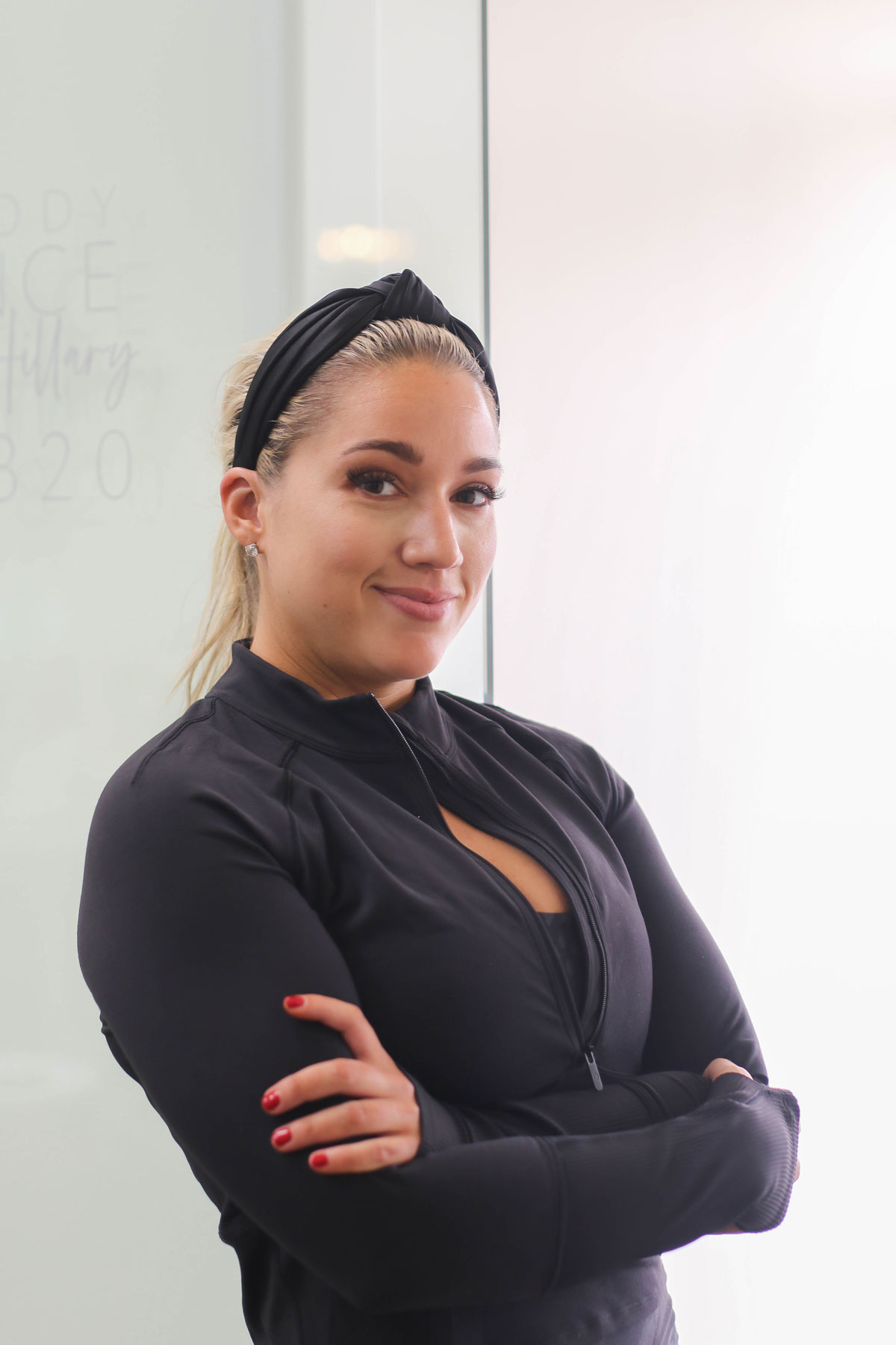 Hillary Goodman wearing black workout clothes, standing next to a window.